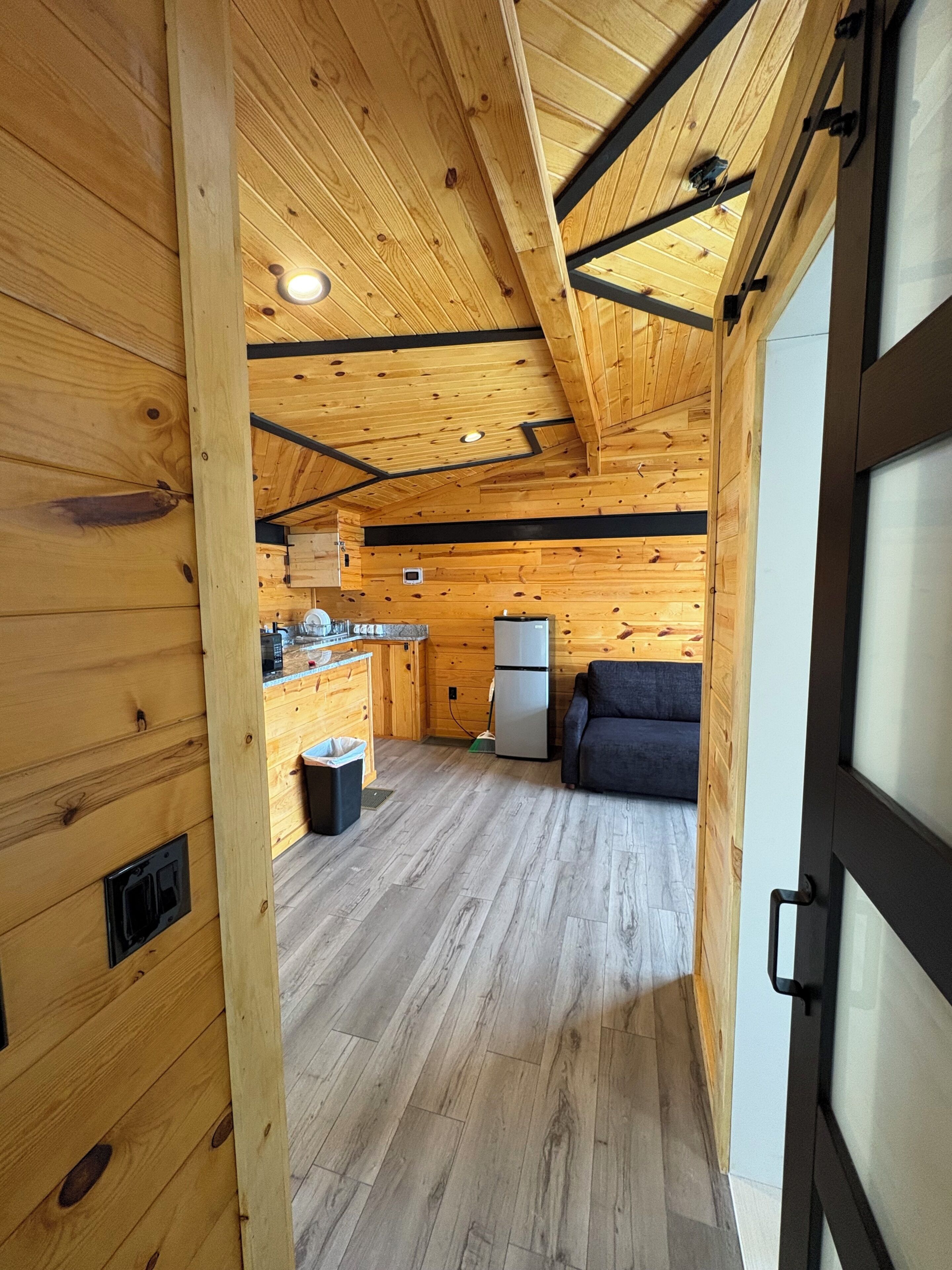 Ein Holzinterieur mit Küchenbereich, einem Kühlschrank, einer Couch und einer Tür mit Griff.