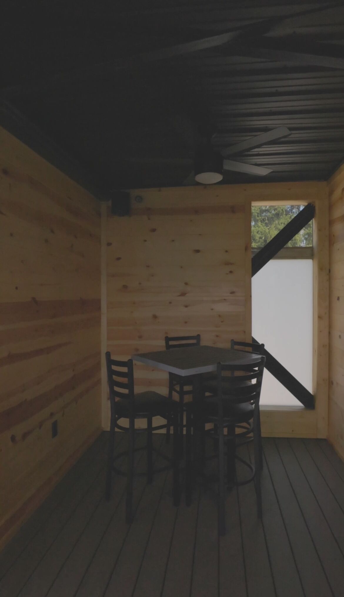 Un interior de madera con una mesa y sillas, techo inclinado y ventana con vistas a vegetación.