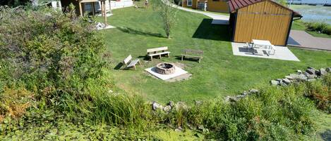 A grassy outdoor area with a fire pit, picnic tables, and a small shed.