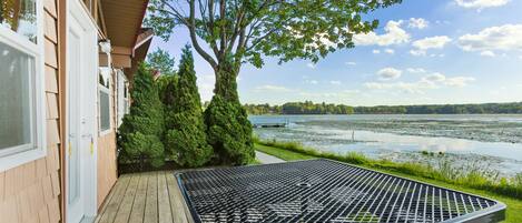 A wooden deck with a metal table and bench, overlooking a lake with trees and a clear sky.