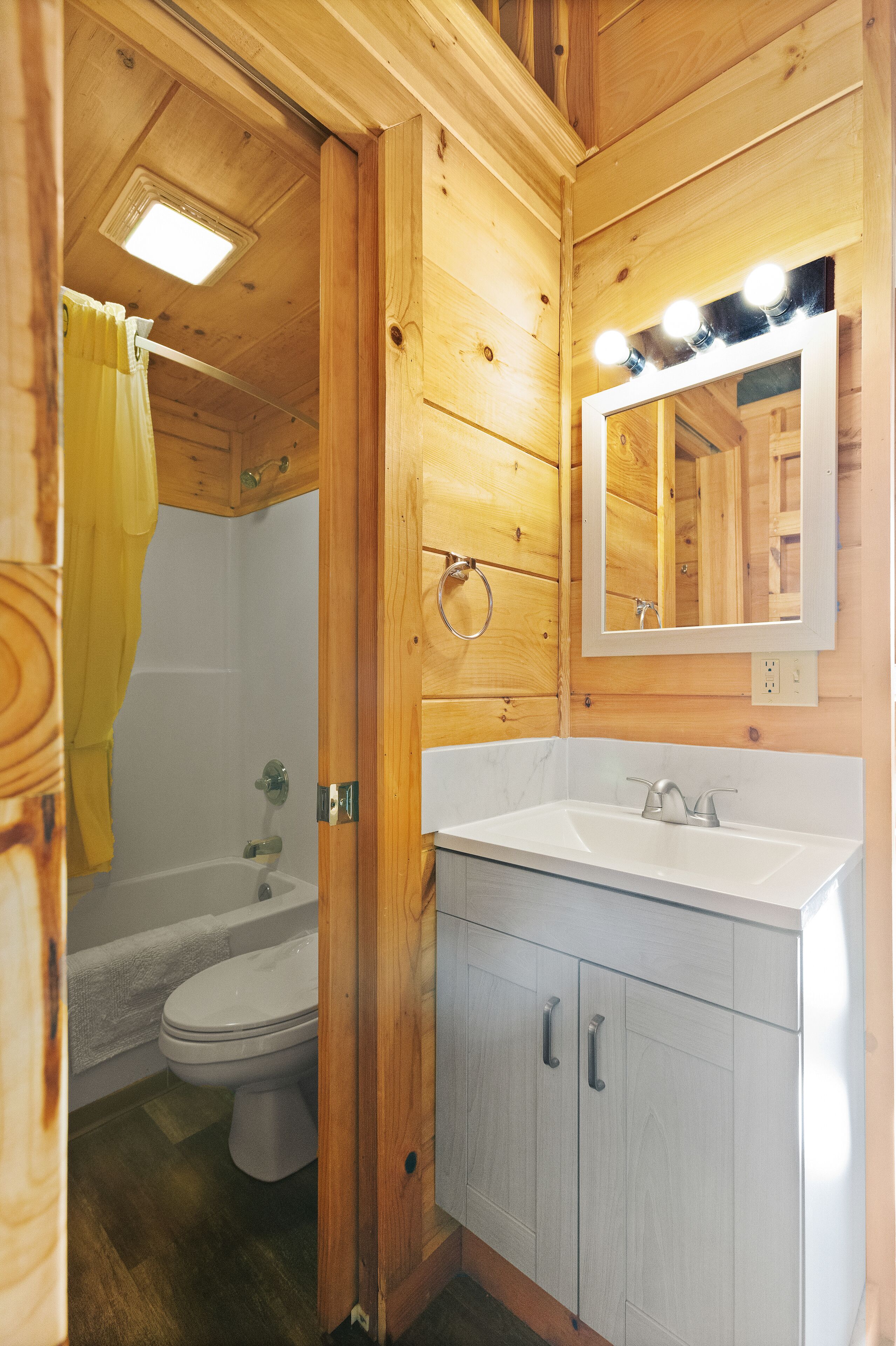 Une salle de bain rustique, avec des murs en bois, un lavabo blanc, un miroir et une douche.