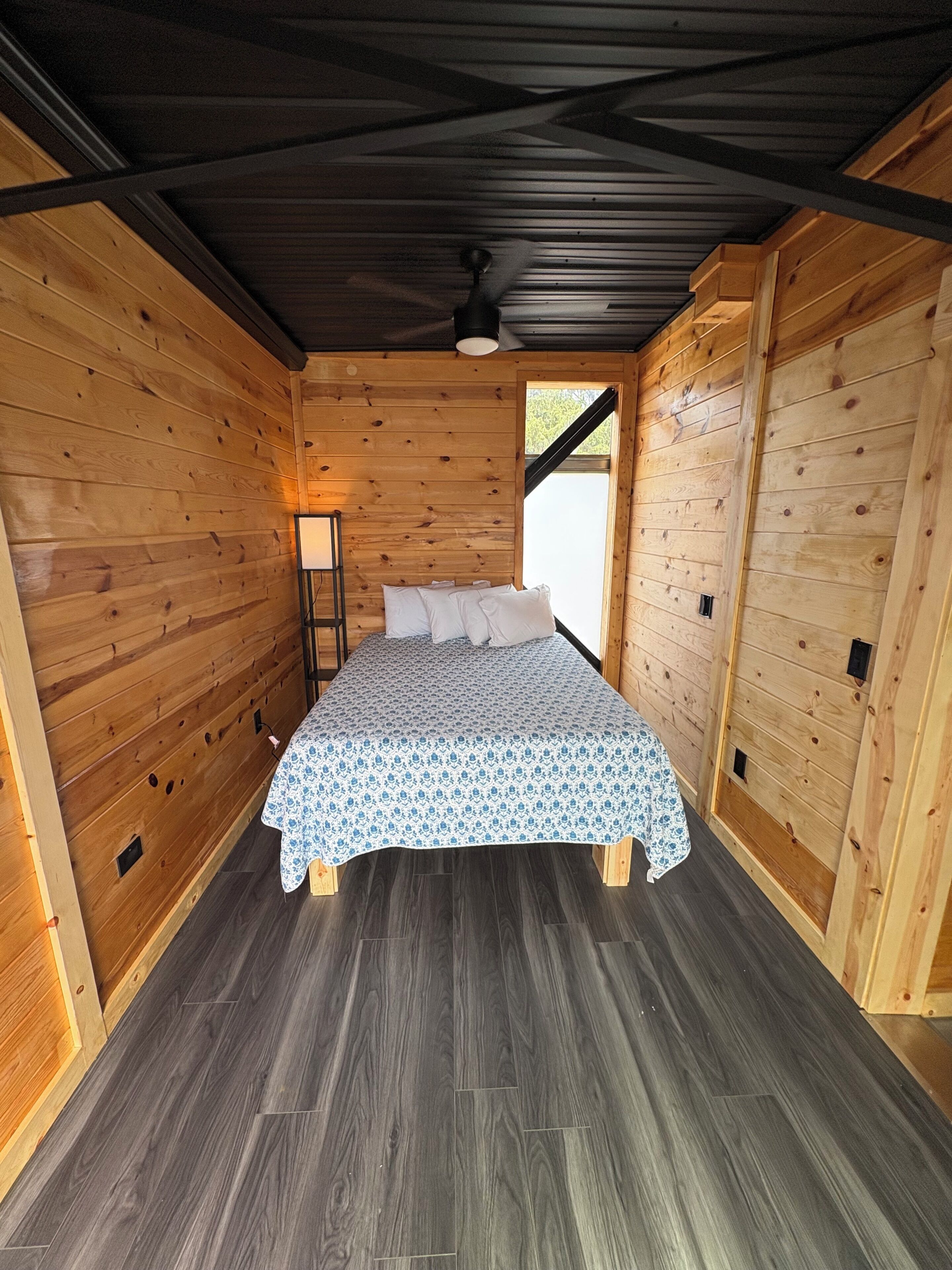 Een houten kamer met een bed, een nachtkastje en een raam.