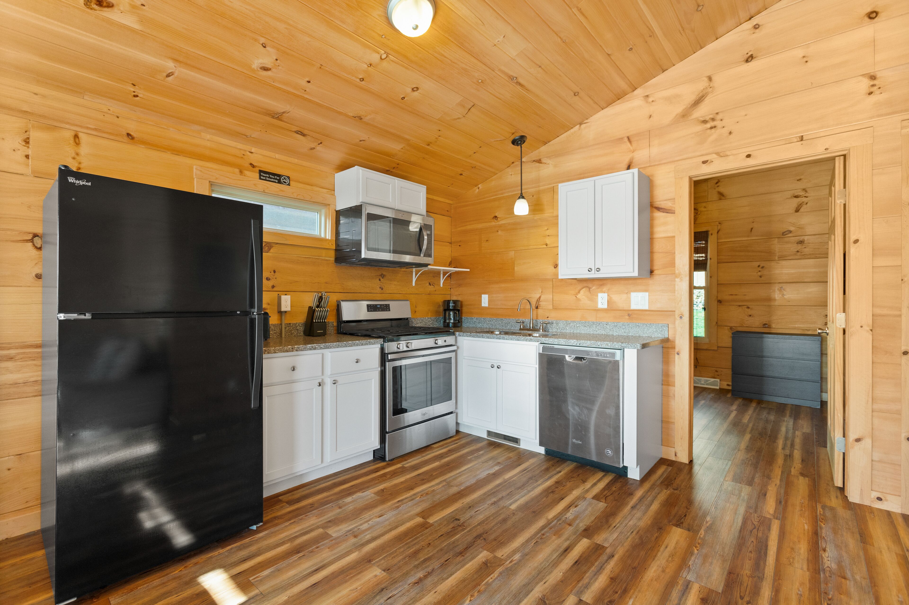 A modern kitchen with wooden walls, a black refrigerator, stainless steel appliances, and a granite countertop.