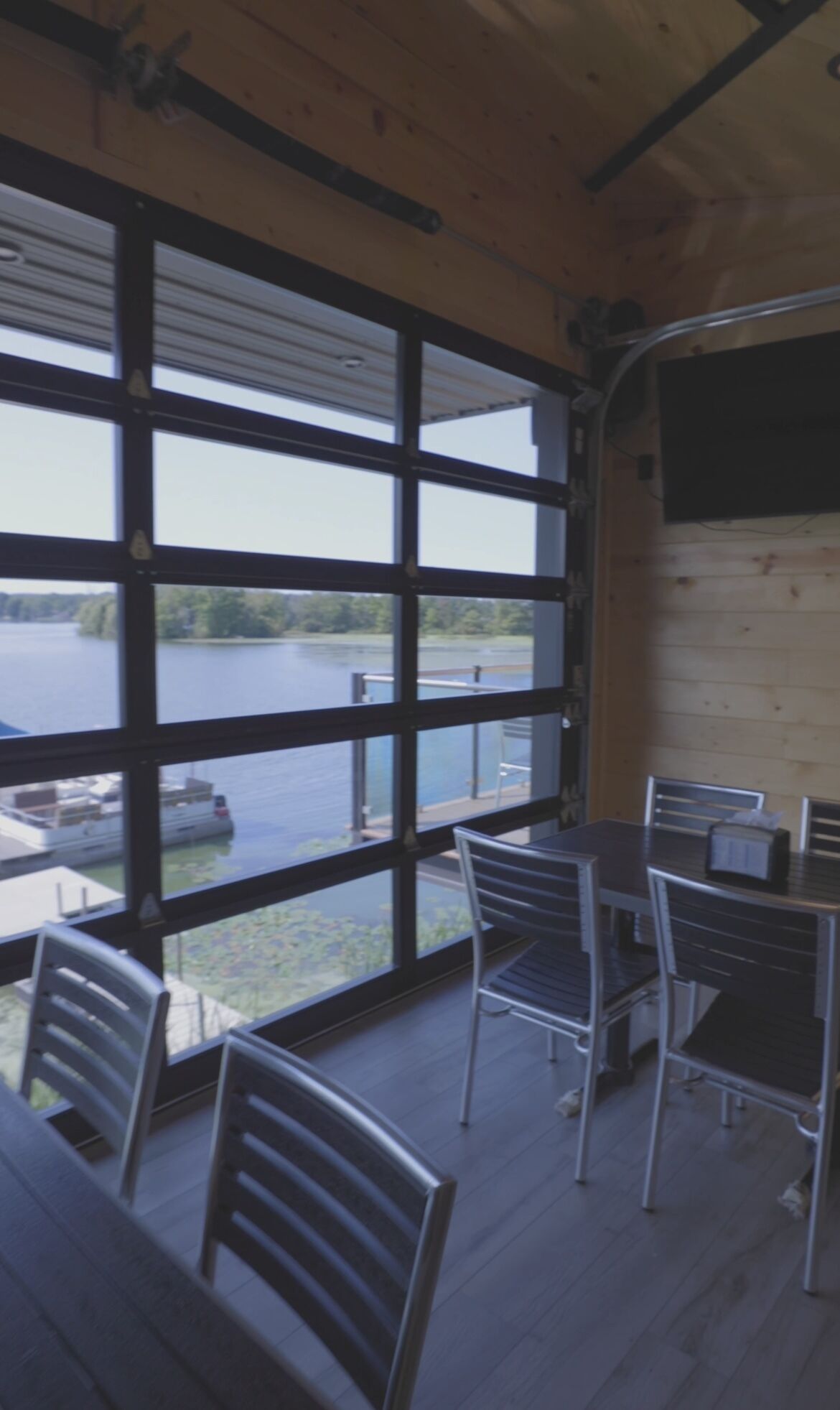 A room with large windows overlooking a lake, metal chairs, and a table.