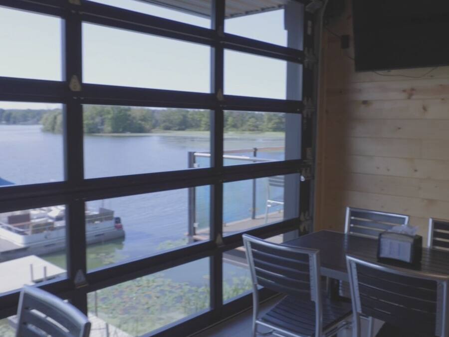 A room with large windows overlooking a lake, metal chairs, and a table.