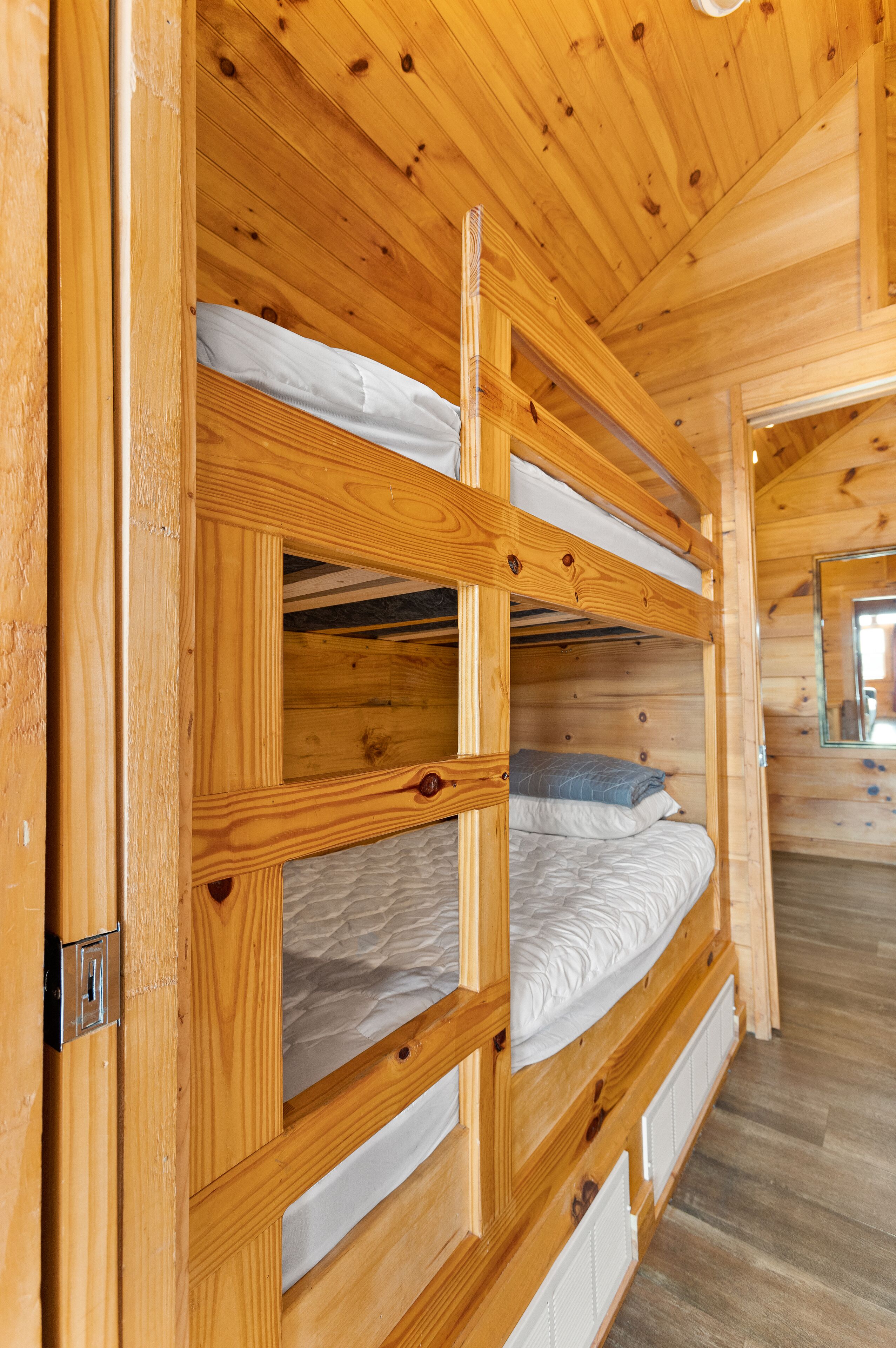 A wooden bunk bed room with a wooden ceiling and walls, a door, and a mirror on the wall.