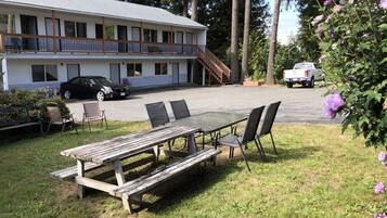 A motel with a covered outdoor seating area, a staircase leading to the upper level, and a parking lot with vehicles.
