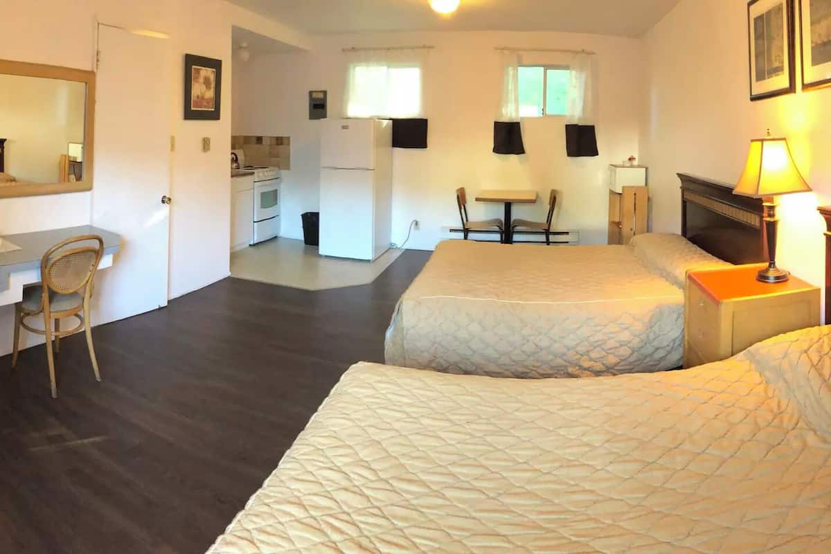 A hotel room with two beds, a desk with a chair, a television, a small kitchen area, and a fireplace.