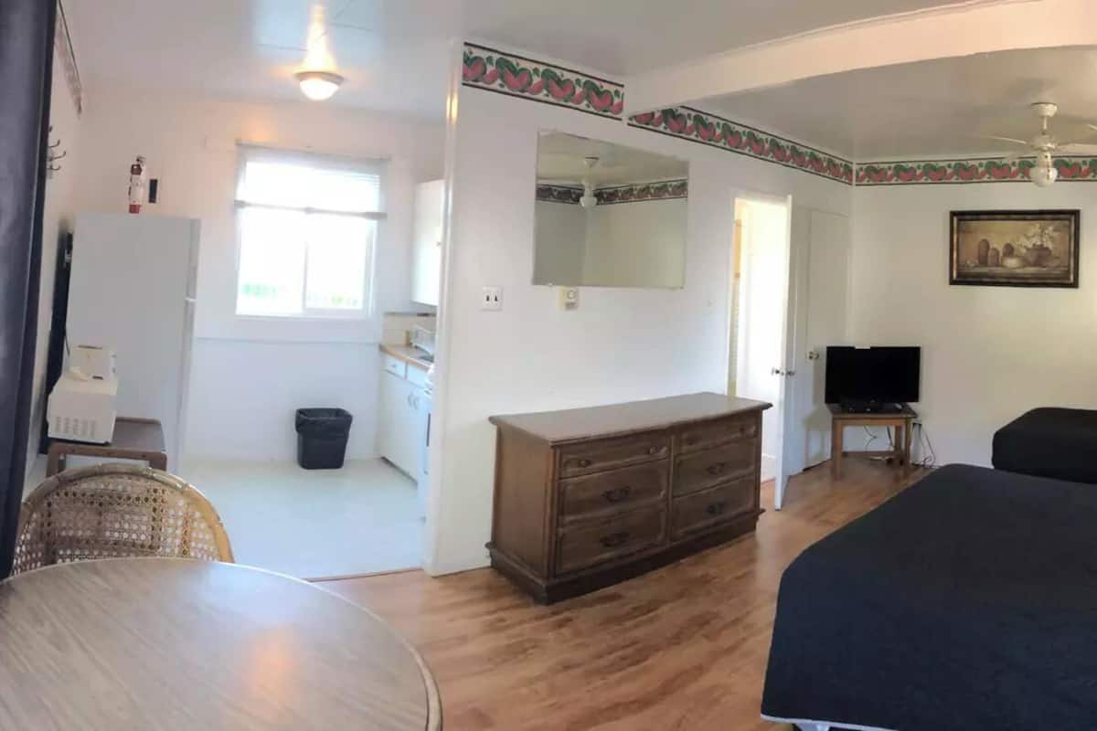A hotel room with a bed, a dresser, a mirror, a television, and a dining area with a table and chairs.