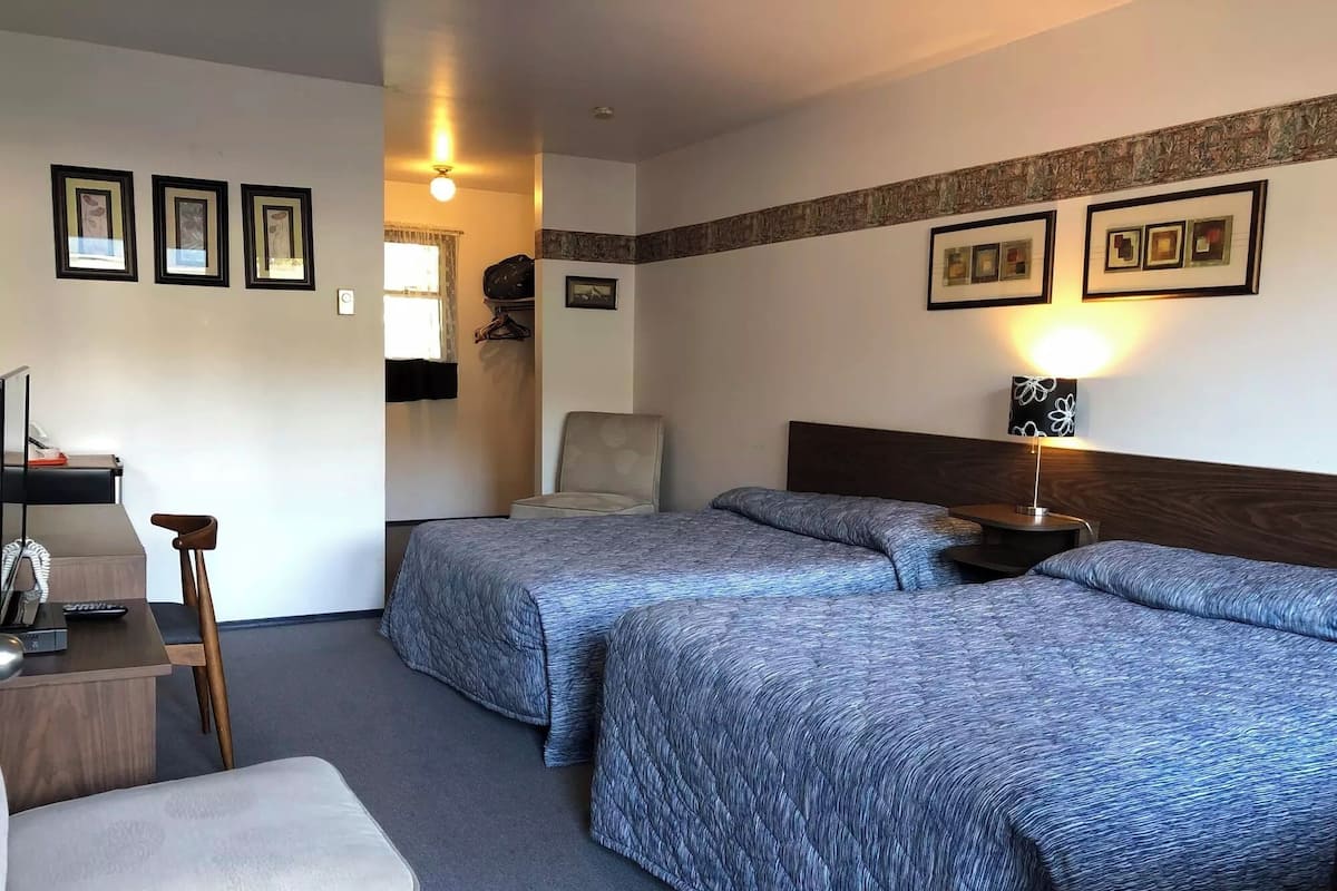 A hotel room with two beds, a desk with a chair, a small table, and a lamp.