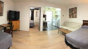 A compact hotel room with two beds, a television on a wooden cabinet, a small table, and a kitchenette in the background. - Marland Motel (Powell River)