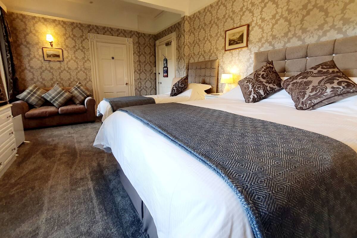 A hotel room with a large bed, a sofa, a dresser, and a door.