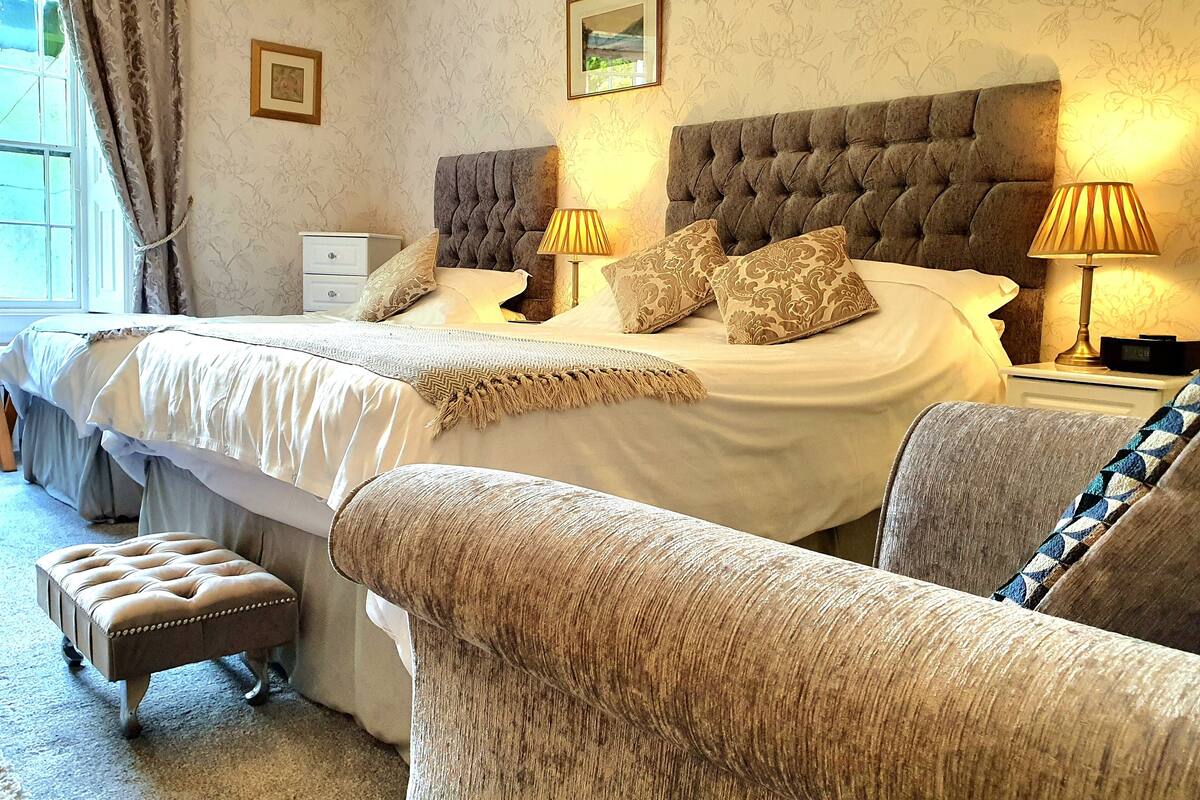 A bedroom with a large bed, two bedside lamps, a nightstand, a chair, and a small table.