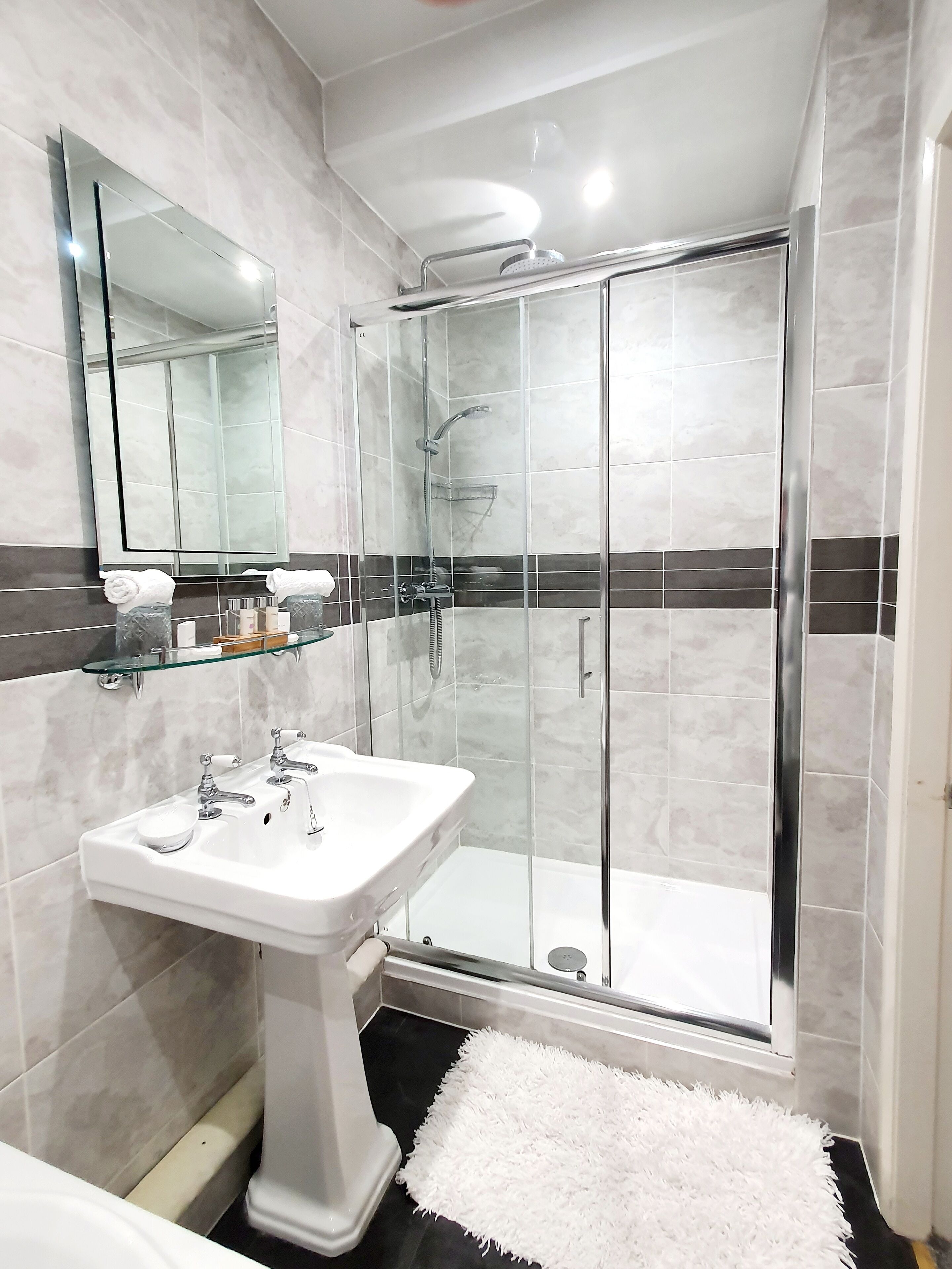 Un baño moderno con cabina de ducha de vidrio, lavamanos pedestal y un espejo grande.
