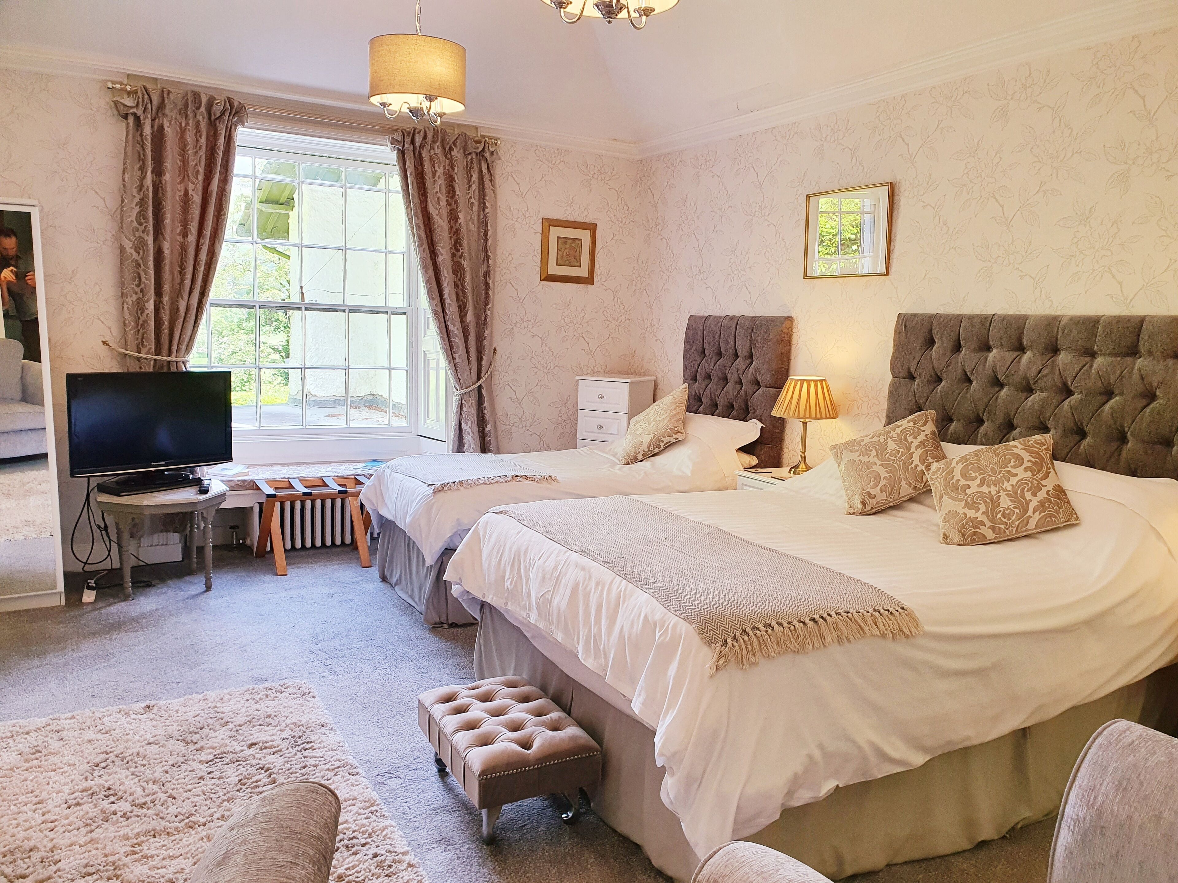A bedroom with two beds, a television, a lamp, and a window with curtains.