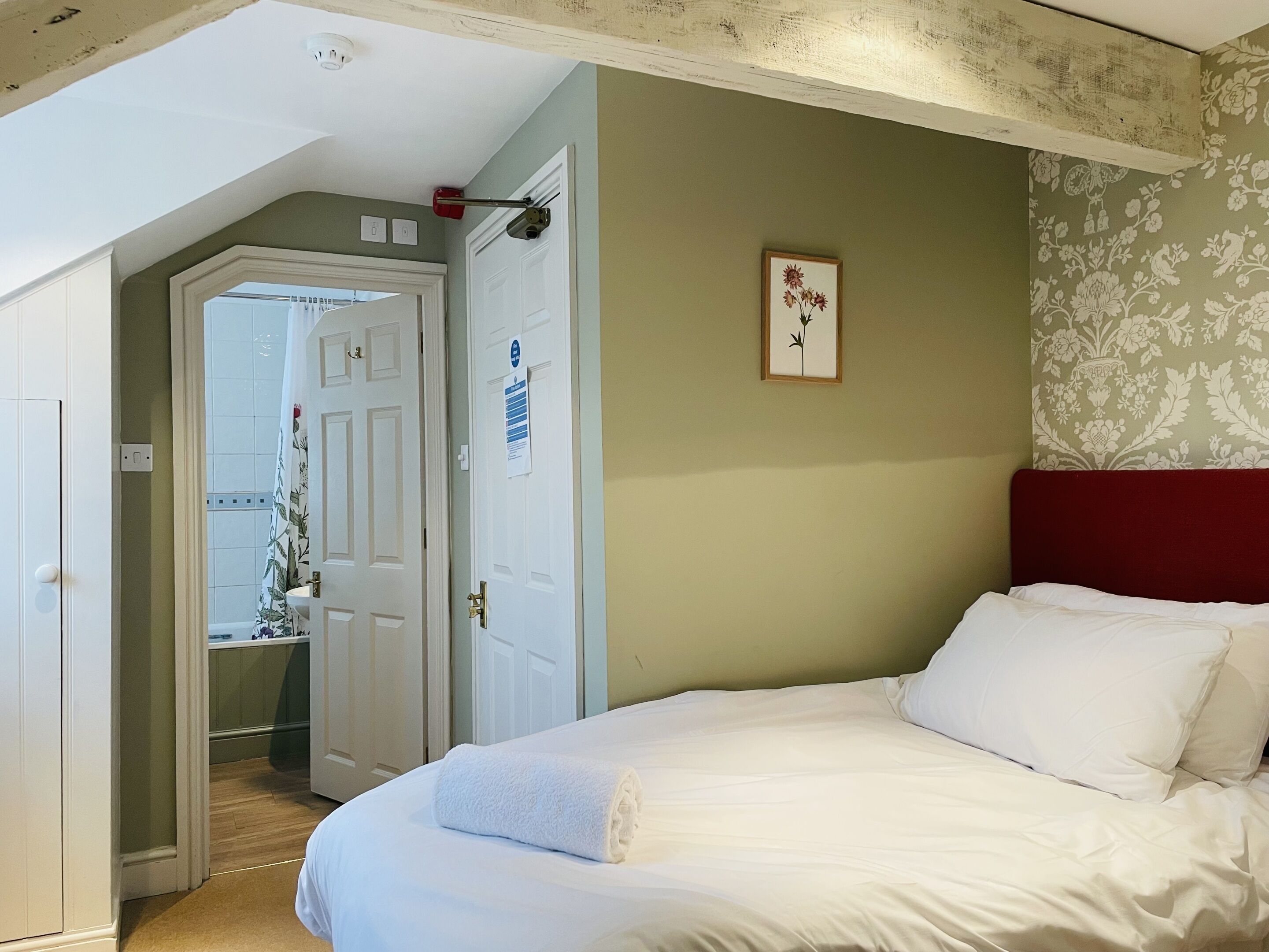Een slaapkamer met een bed, een deur naar een badkamer en een wand met een bloemendesign.