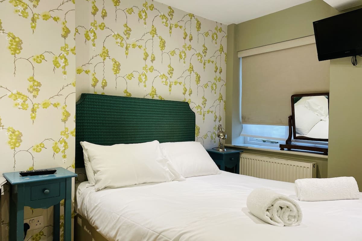 A hotel room with a bed, a nightstand, a lamp, a TV, and a window with a view.