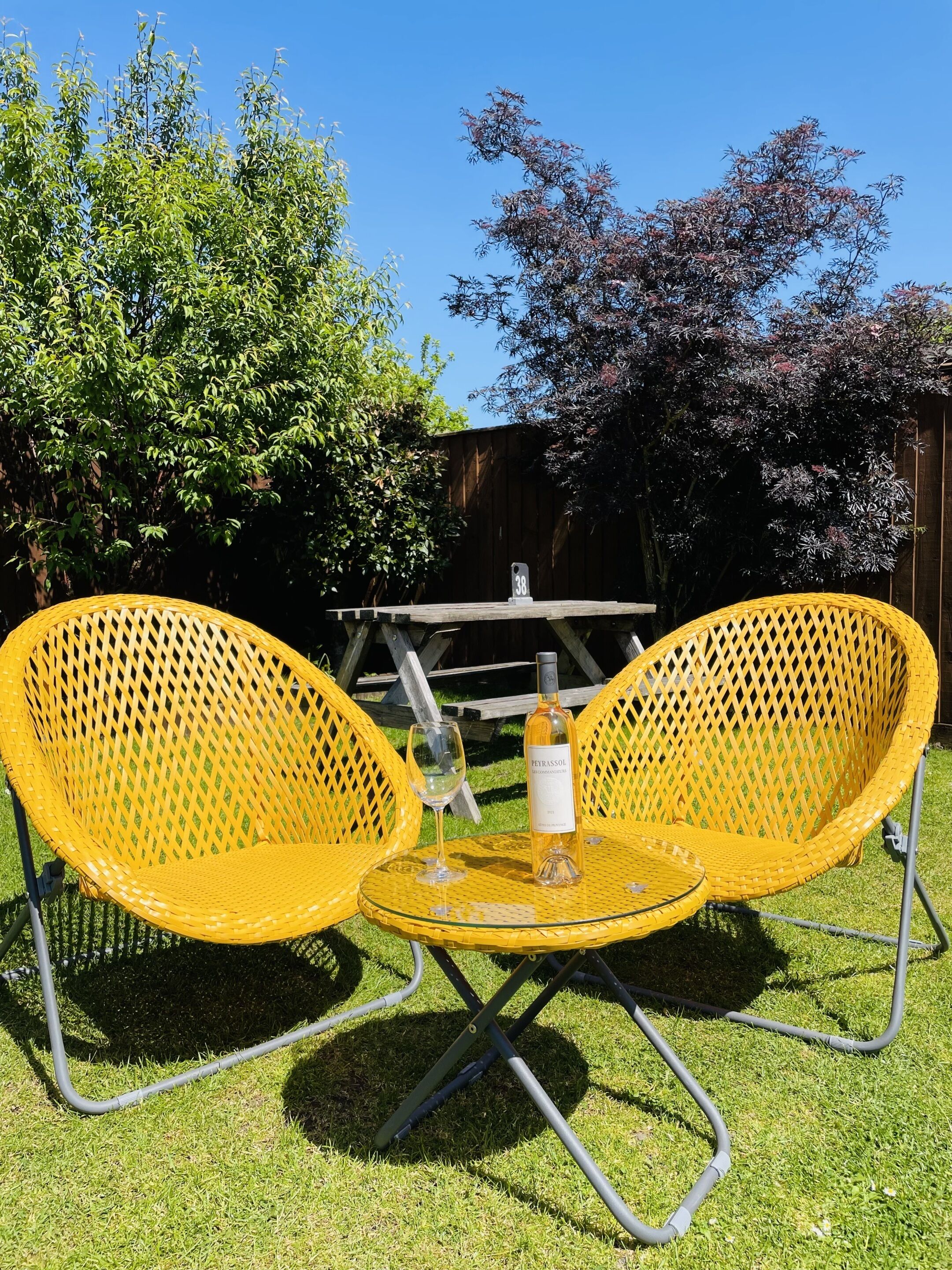 A yellow outdoor seating area with a table and chairs, a bottle of wine, and a number 38 sign.