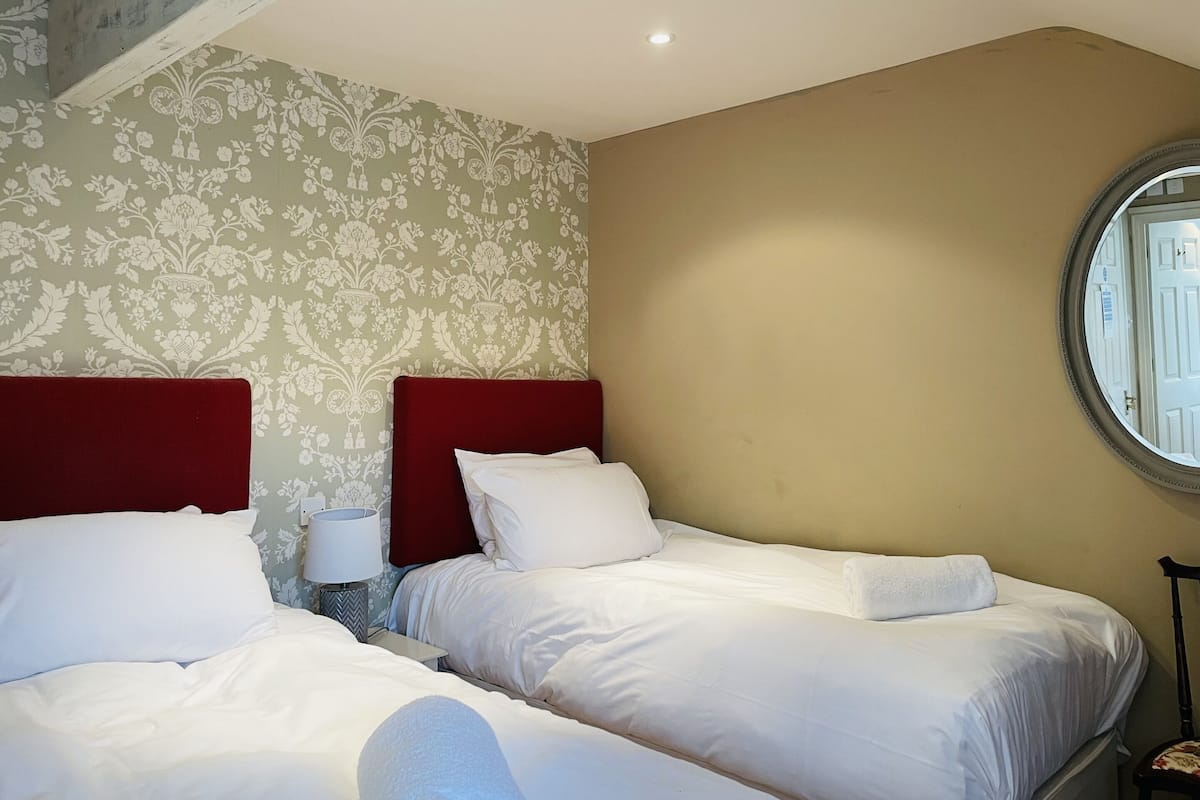 A hotel room with two beds, a nightstand, a lamp, and a window with a view.