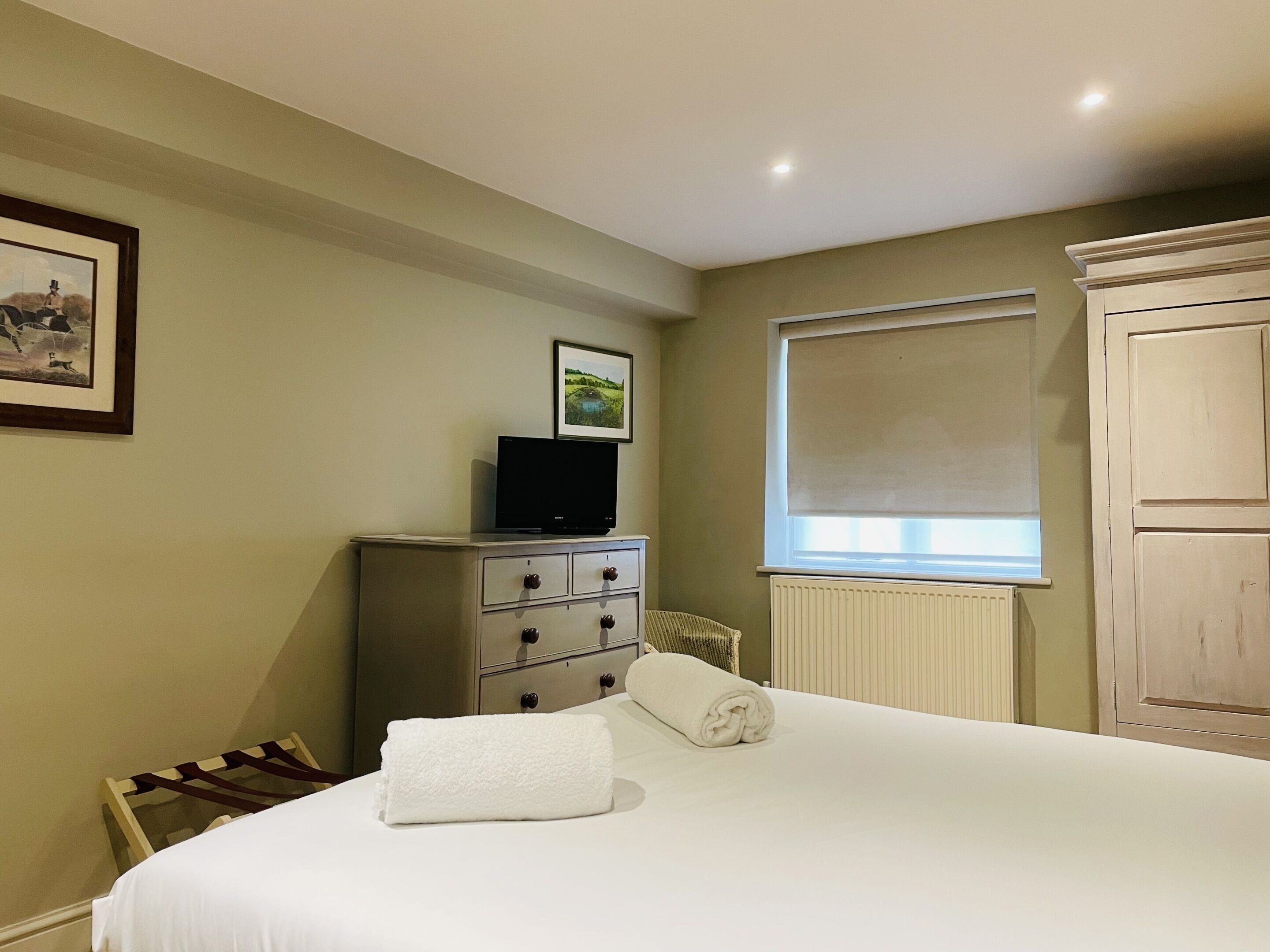 A hotel room with a bed, a dresser, a television, and a window with a blind.