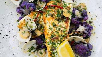 A plate of food with clams, cauliflower, and a piece of fish, garnished with herbs and lemon.