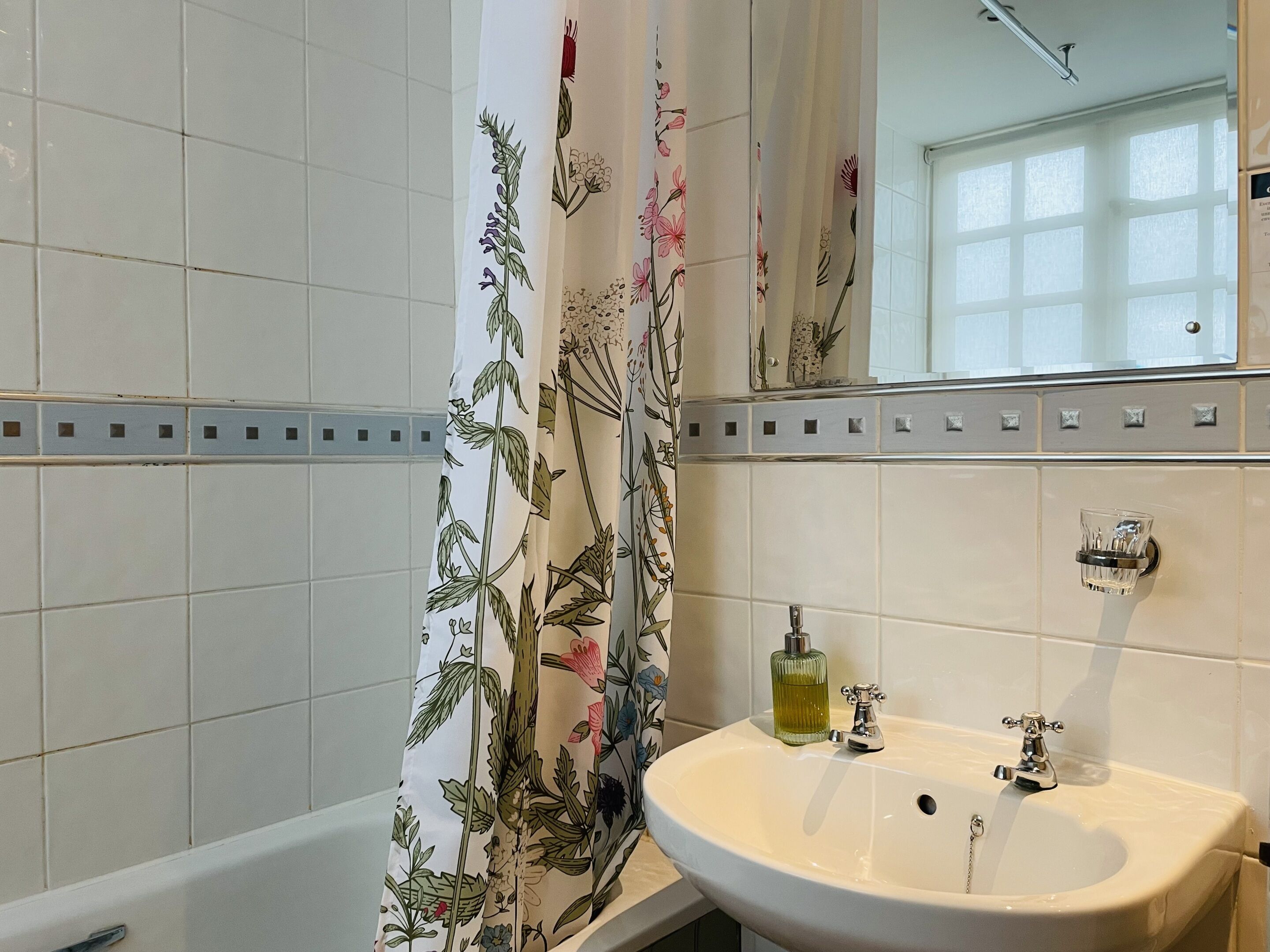 Ein Badezimmer mit einem weißen Waschbecken, einem Spiegel und einer Duschvorhang mit Blumenmuster.