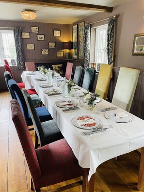 A dining room with a long table set for a meal, surrounded by upholstered chairs with patterned upholstery. - Greyhound Inn (Dorchester)