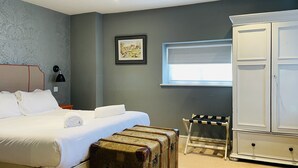 A bedroom with a bed, a nightstand, a lamp, a wardrobe, a window, and a suitcase.