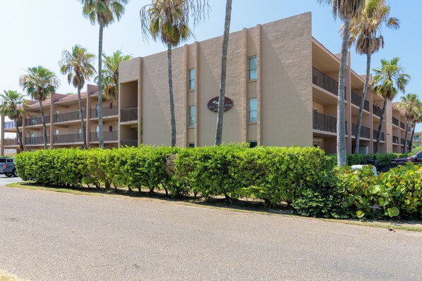 A multi-story hotel with a beige facade, palm trees, and a well-maintained hedge along the street. - Beachview by South Padre Condo Rentals (South Padre Island)