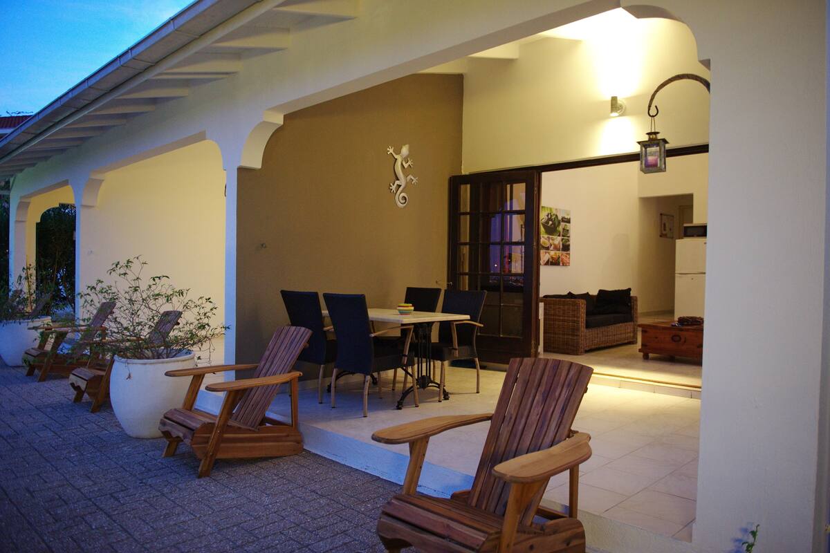 Un patio al aire libre con sillas y una mesa de madera, una planta en maceta y una lámpara fijada a la pared.