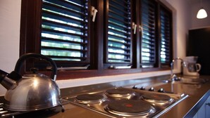 A kitchen with a stove, kettle, and window blinds. - Bantopa Apartments & Villas (Sint Michiel)