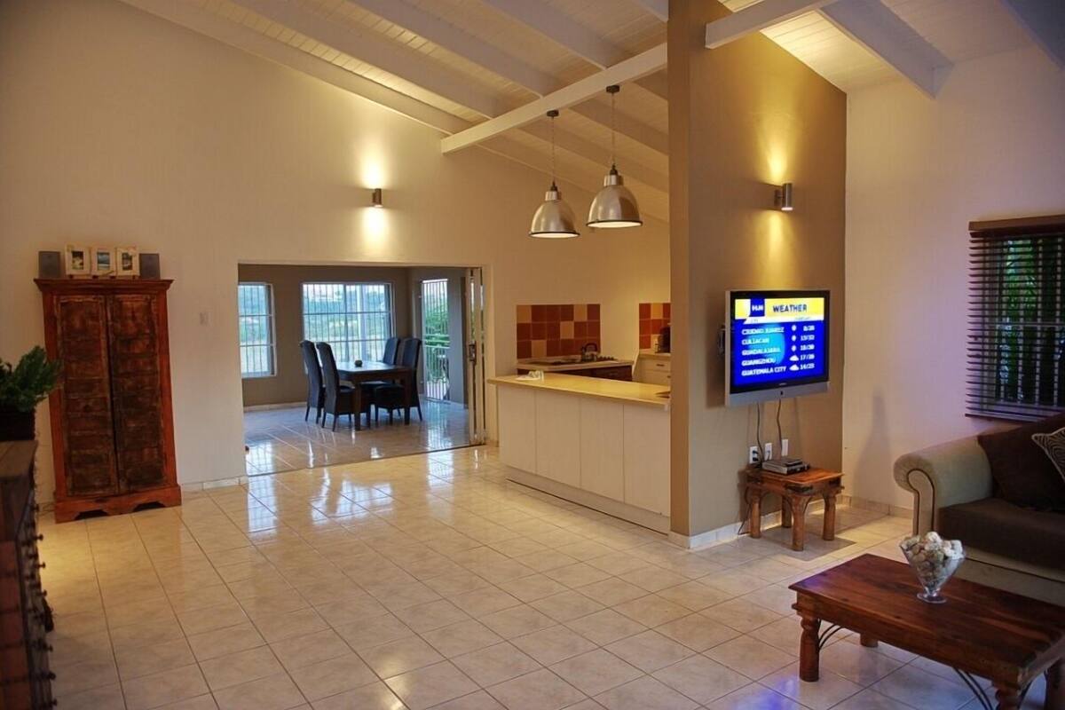 Amplia sala de estar con comedor, cocina y televisor mostrando información meteorológica.