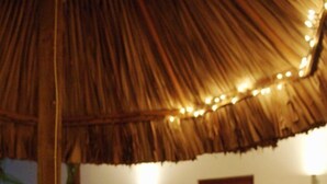 A wooden dining table with chairs, a thatched roof, string lights, and a painting on the wall. - Bantopa Apartments & Villas (Sint Michiel)