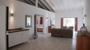 A spacious living area with a high ceiling, a kitchen with white cabinets, a wicker sofa, and a dining area with a table and chairs. - Bantopa Apartments & Villas (Sint Michiel)