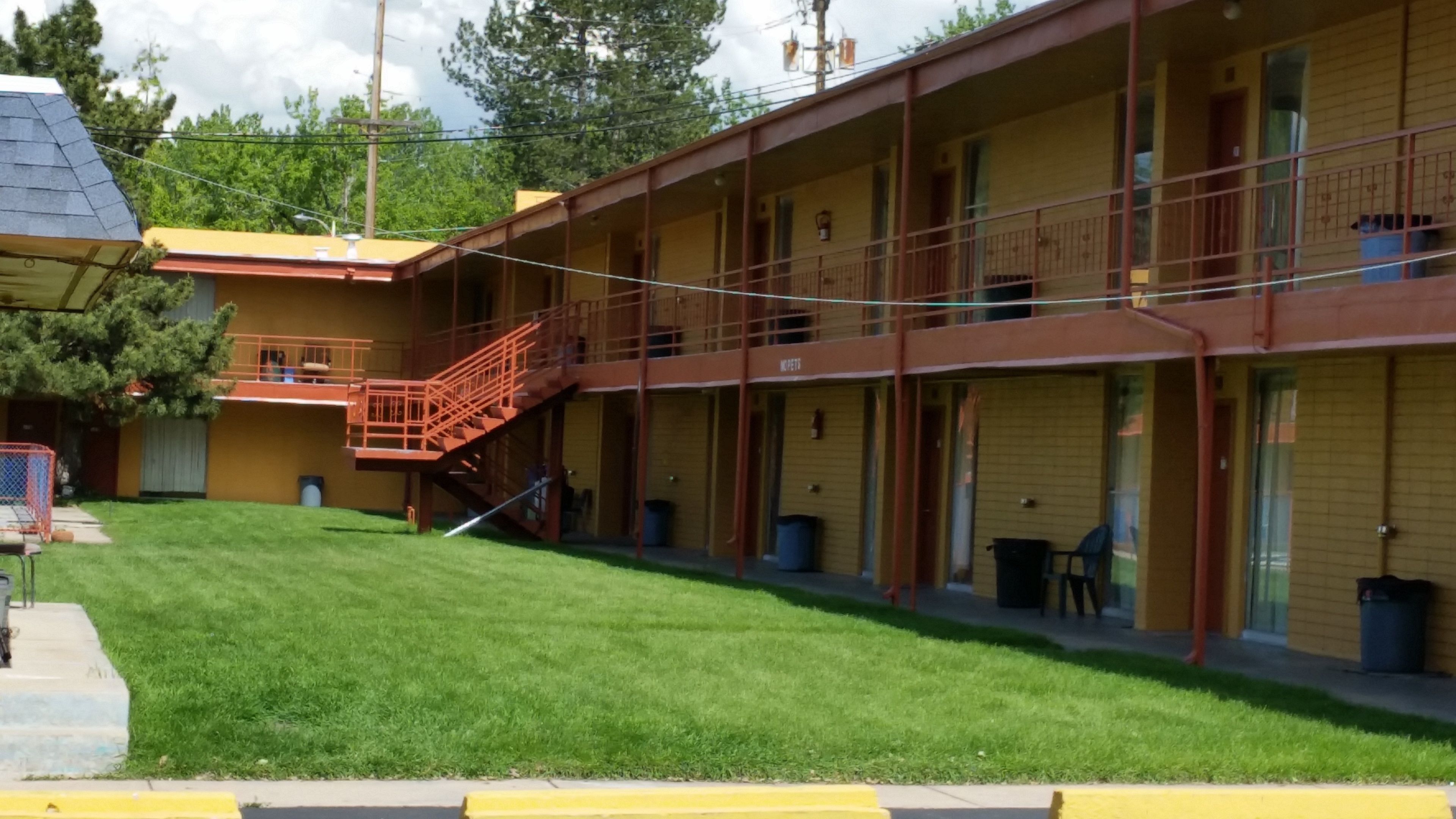 A motel with a two-story structure, a staircase leading to the upper level, and a well-maintained lawn in front.