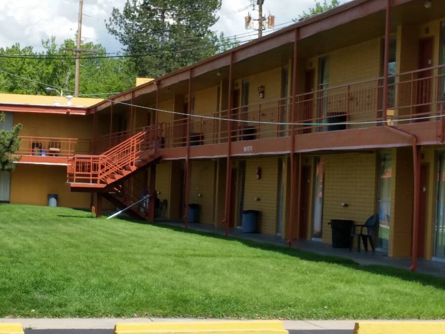 A motel with a two-story structure, a staircase leading to the upper level, and a well-maintained lawn in front.