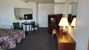 A hotel room with a bed, a desk with a telephone, a chair, a dresser with a television, and two lamps. - Essex House Motel (Littleton)