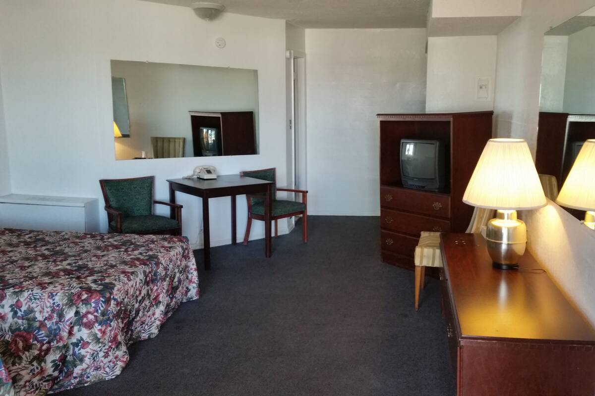 Ein Hotelzimmer mit einem Bett, einem Schreibtisch mit Telefon, einem Sessel, einer Kommode mit Fernseher und zwei Lampen.