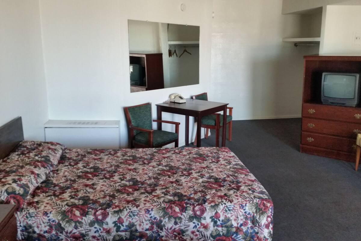 Ein Hotelzimmer mit einem Bett, einem Schreibtisch mit Stuhl, einem Fernseher und einem Kleiderschrank.