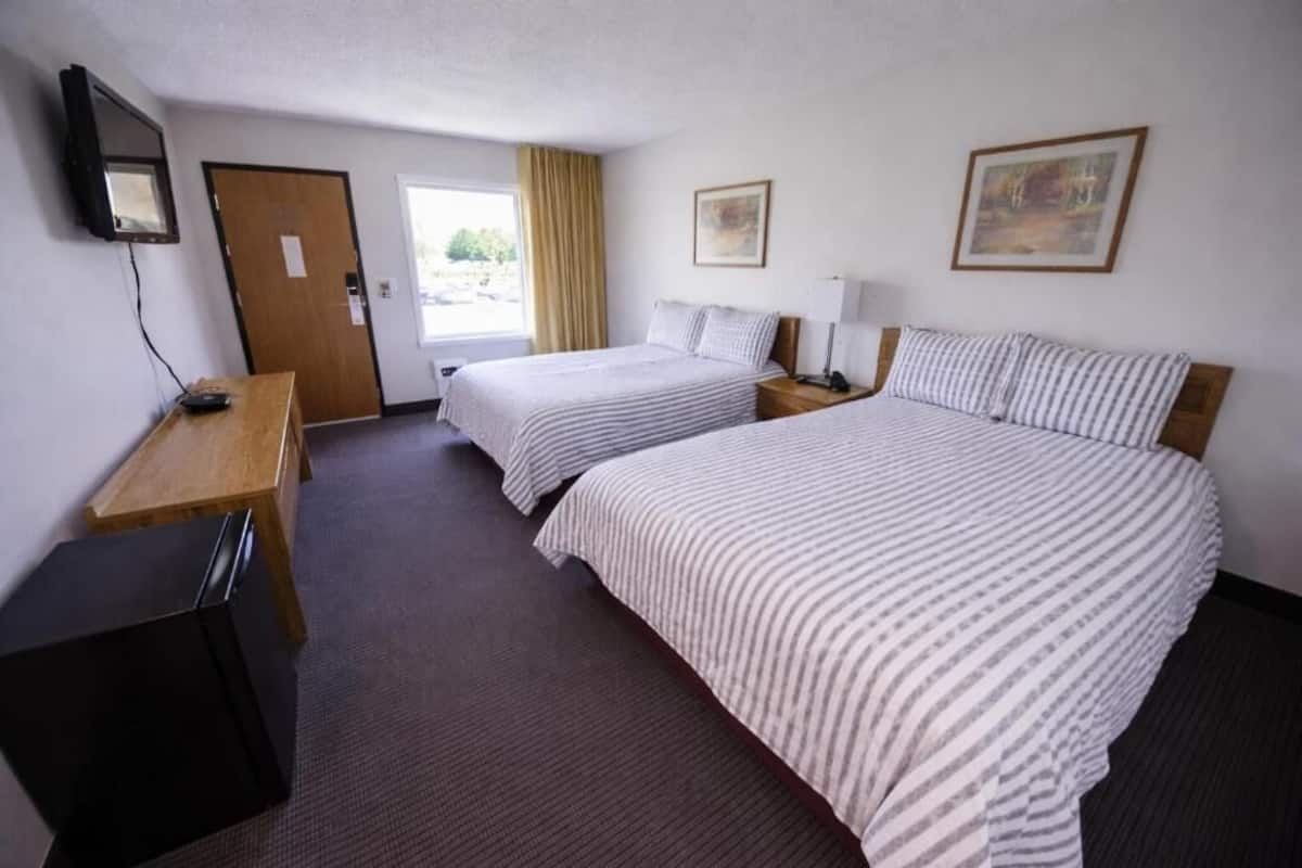 Una habitación de hotel con dos camas, un escritorio, un televisor y una puerta.
