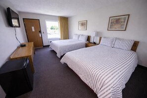 A hotel room with two beds, a desk, a TV, and a door. - Westwood Inn & Suites (Kimball)