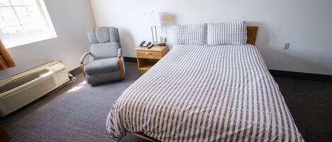 Una habitación de hotel con cama, una silla, una mesita de noche con lámpara y ventana.