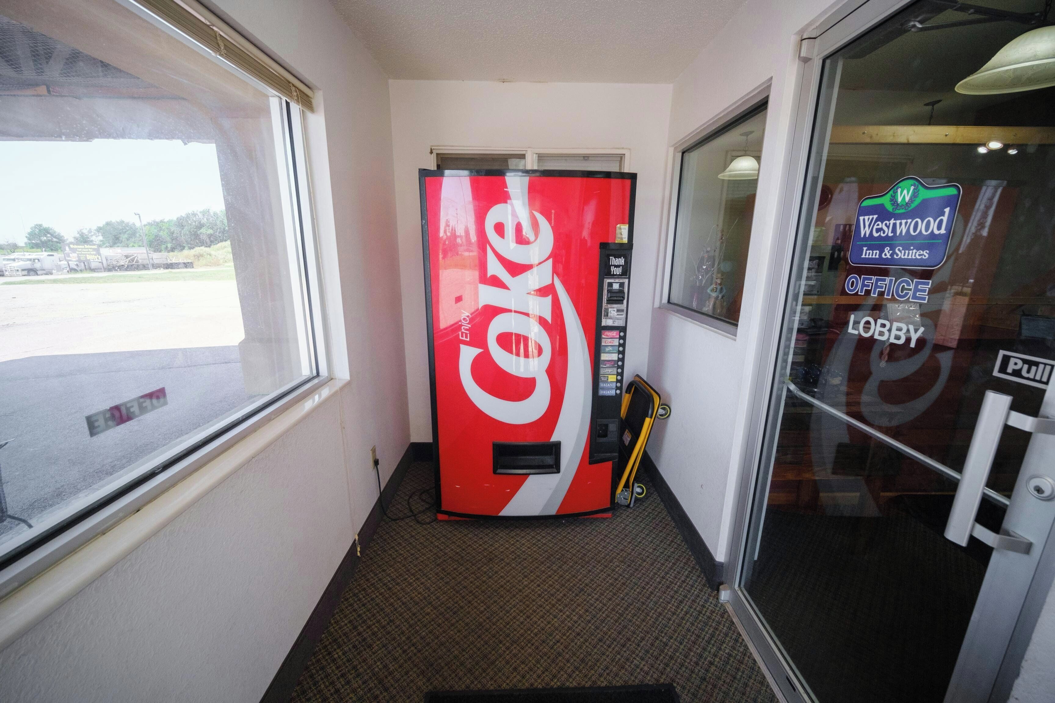 A Coca-Cola vending machine in a hallway with a Westwood Inn & Suites sign in the background.