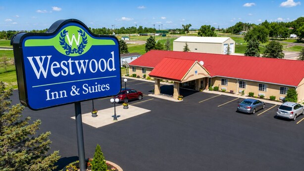 Un hôtel Westwood Inn & Suites avec un bâtiment à toit rouge, un parking et un panneau d’affichage portant un logo.