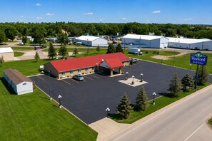 A Westwood Inn & Suites with a red-roofed building, a parking lot, and surrounding industrial buildings. - Westwood Inn & Suites (Kimball)