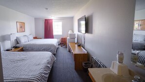 Une chambre d’hôtel avec deux lits, un bureau, une télévision, un miroir, une fenêtre avec des rideaux et un lavabo.