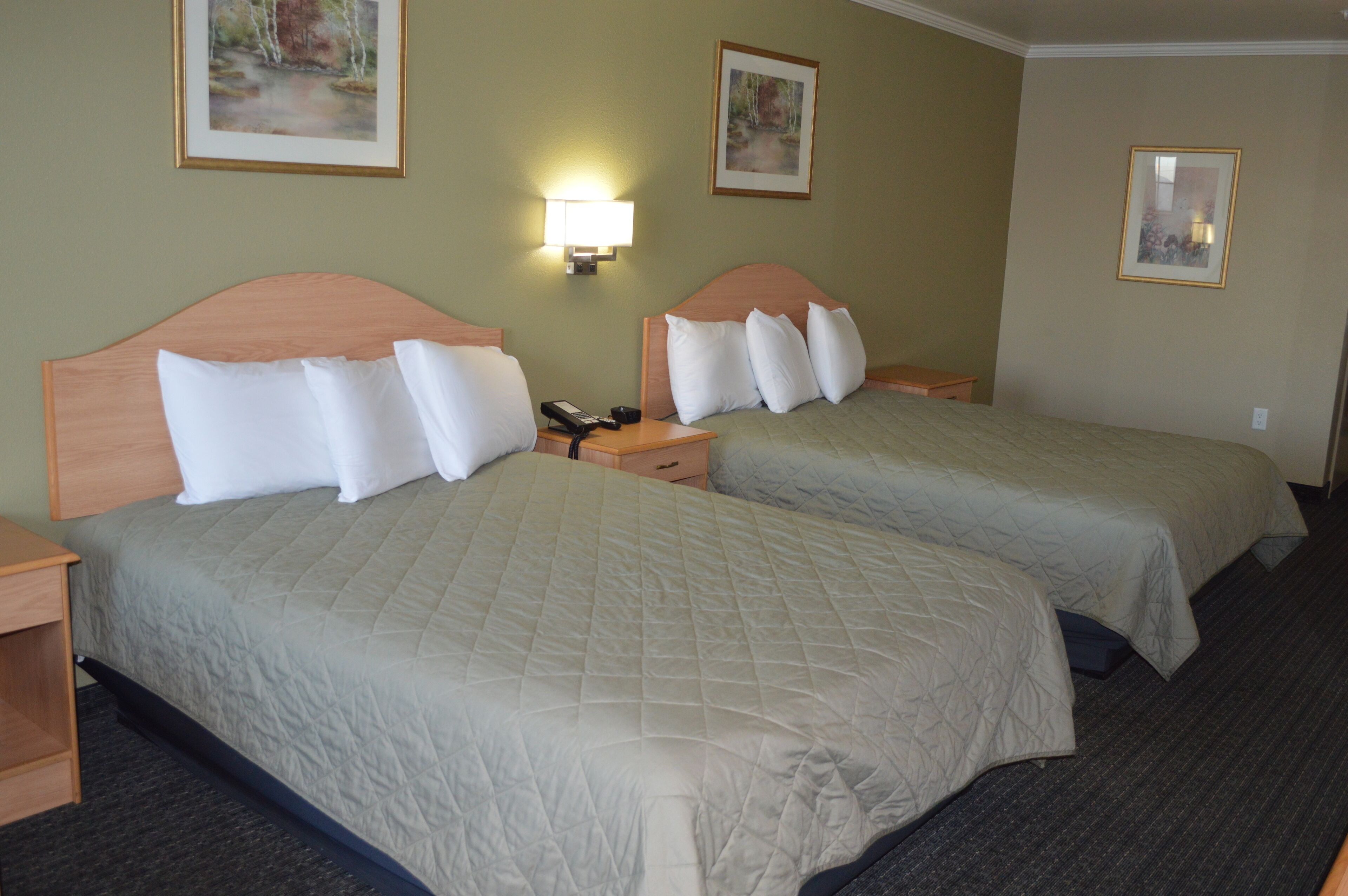 A hotel room with two beds, a nightstand with a phone, and wall-mounted lamps.