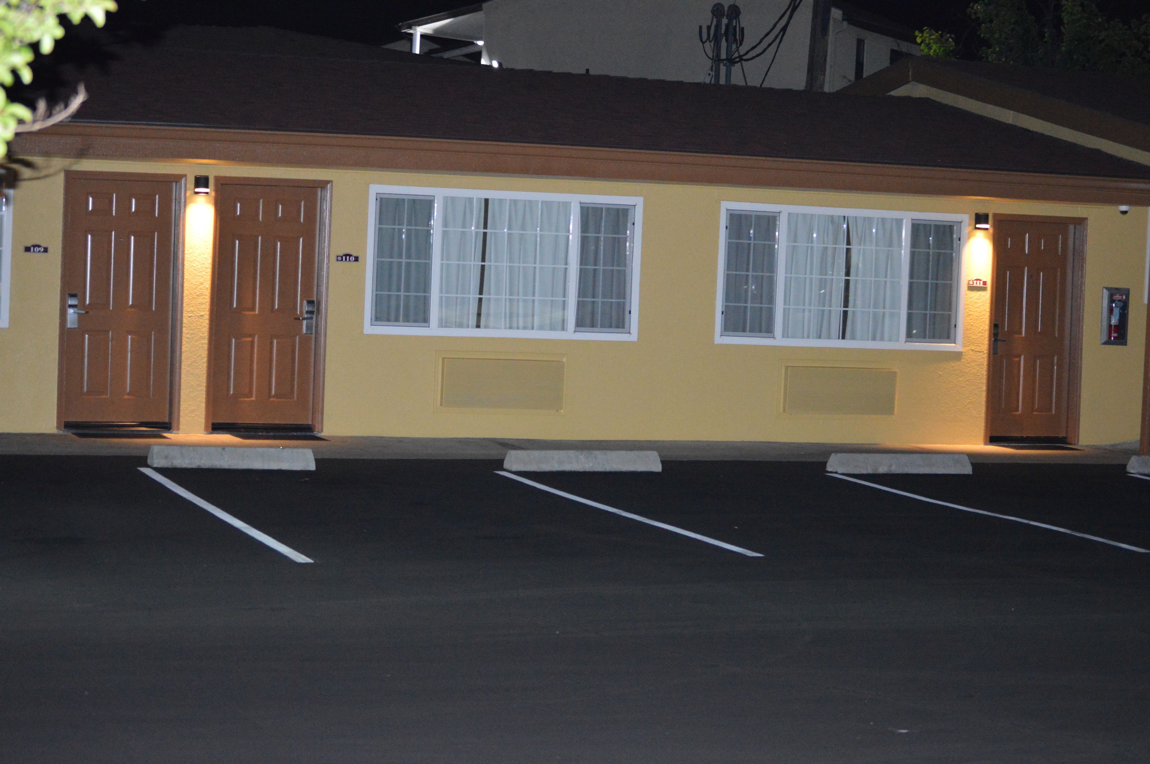 Un edificio con dos puertas y ventanas, un estacionamiento con espacios delimitados y un letrero pequeño en la pared.