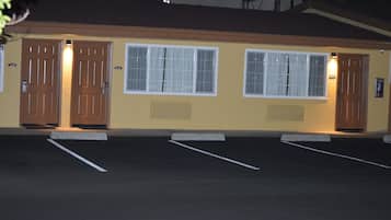 Un edificio con dos puertas y ventanas, un estacionamiento con espacios delimitados y un letrero pequeño en la pared.