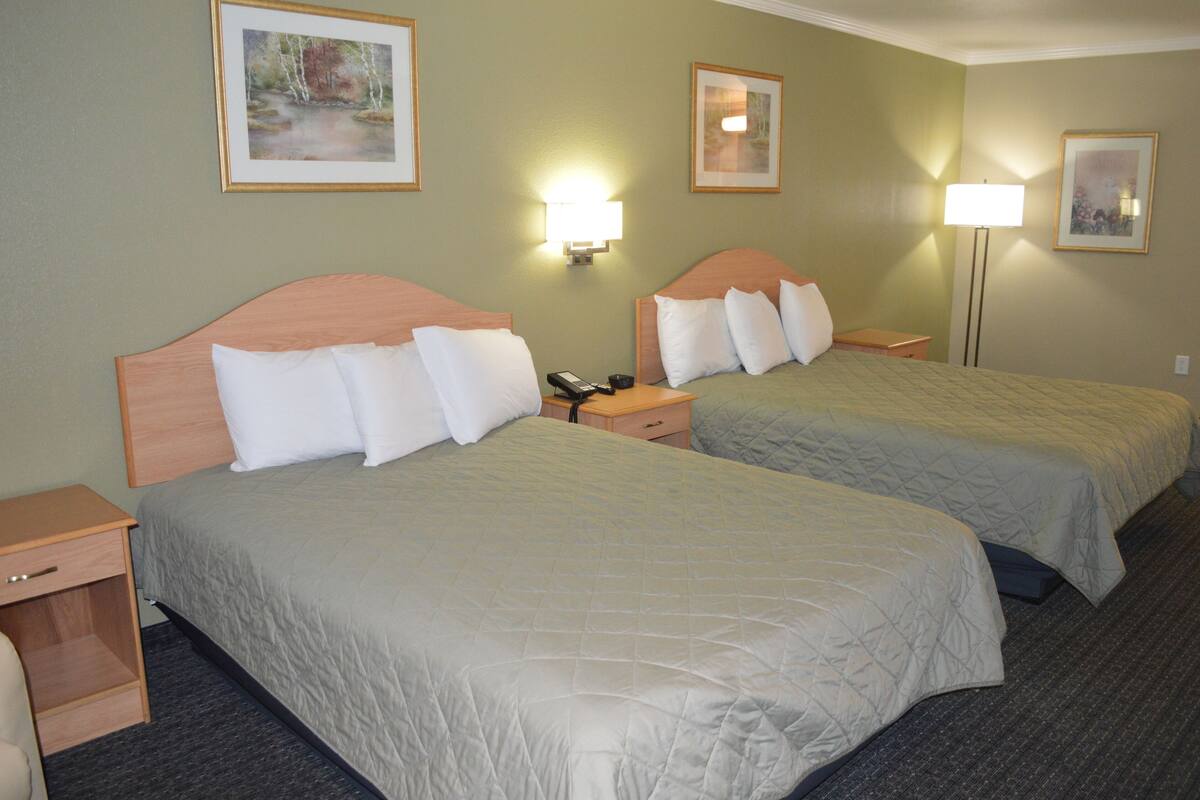 A hotel room with two beds, bedside lamps, and a nightstand with a phone.